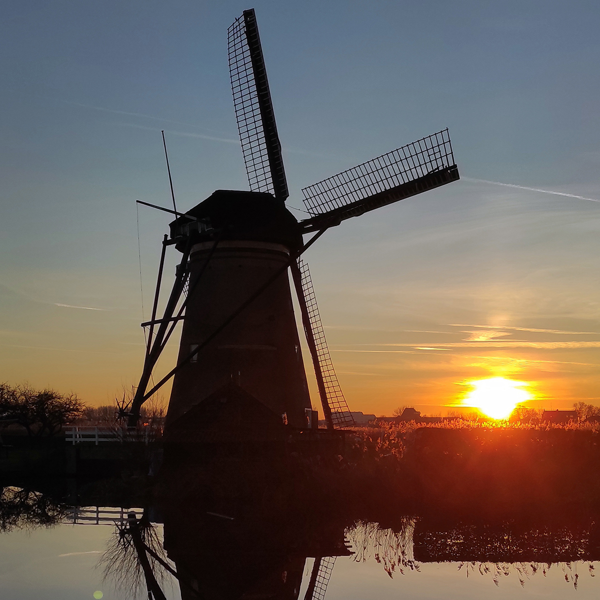 Einzelne Windmühle vor Gewässer bei Sonnenuntergang